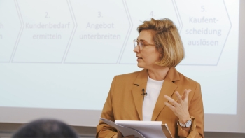 Lehrerin steht vor der an die Wand projizierten Präsentation und schaut nach links.