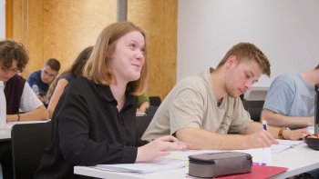 Schülerin lächelt. Im Hintergrund sind Schüler:innen die arbeiten.