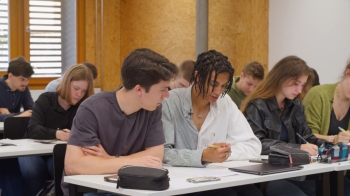 Auf dem Foto sind zwei Schüler zu sehen, die mit der Bearbeitung zu sehen sind. Dabei sind sie einander zugewandt.