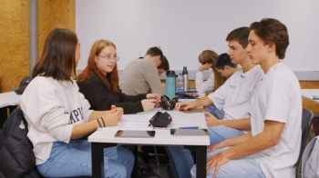 Auf dem Foto ist im Vordergrund eine Gruppe von vier Schüler:innen zu sehen. Im Hintergrund ist auch eine Gruppe von ebenfalls vier Schüler:innen.