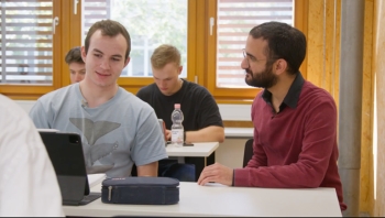 Auf dem Foto ist zu sehen, wie sich der Lehrer mit einem Schüler unterhält.