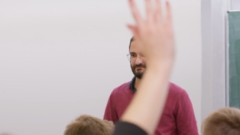 Auf dem Foto ist der Lehrer verdeckt von einer Hand eines/r Schülers/in, die sich meldet.