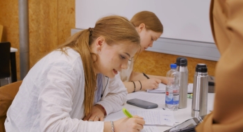 Auf dem Bild sind zwei Schülerinnen zu sehen, die auf einem Blatt Papier mit einem Stift arbeiten.