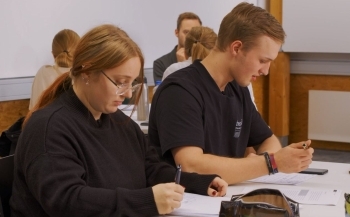 Auf dem Bild sind zwei Schüler:innen zu sehen, die mit einem Stift auf einem Blatt schreiben.